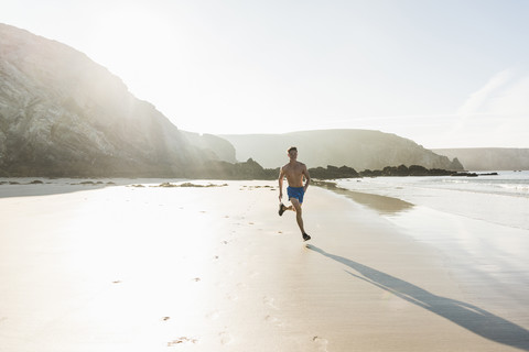 Frankreich, Halbinsel Crozon, junger Mann läuft am Strand, lizenzfreies Stockfoto