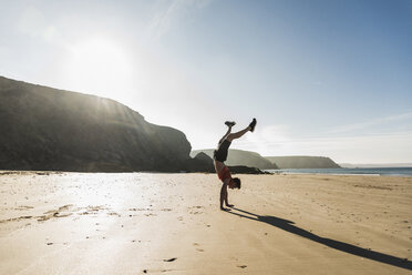 Frankreich, Halbinsel Crozon, junger Mann macht einen Handstand am Strand - UUF08632