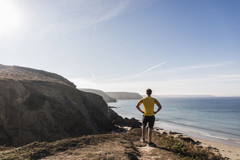 Frankreich, Halbinsel Crozon, sportlicher junger Mann an Steilküste mit Blick auf die Aussicht, lizenzfreies Stockfoto