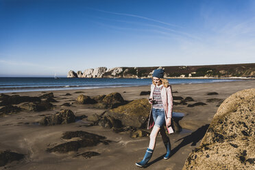 France, Crozon peninsula, teenage girl with cell phone walking on the beach - UUF08644
