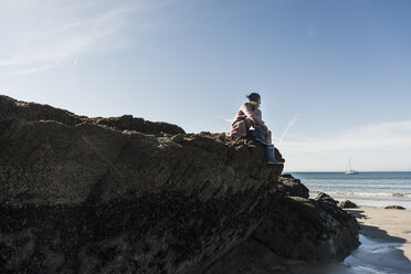 France, Crozon peninsula, teenage girl sitting on rock at the beach - UUF08650