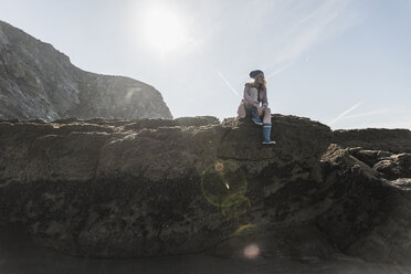 Frankreich, Halbinsel Crozon, junges Mädchen sitzt auf einem Felsen am Strand - UUF08651