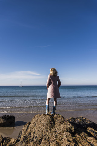 Frankreich, Halbinsel Crozon, junges Mädchen steht auf einem Felsen am Strand, lizenzfreies Stockfoto