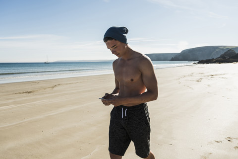 Frankreich, Halbinsel Crozon, junger Mann mit Mobiltelefon am Strand, lizenzfreies Stockfoto