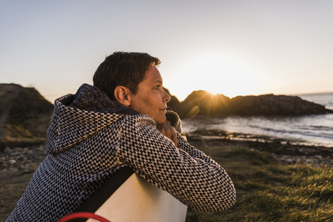 Frankreich, Bretagne, Halbinsel Crozon, Frau an der Küste bei Sonnenuntergang mit Surfbrett, lizenzfreies Stockfoto