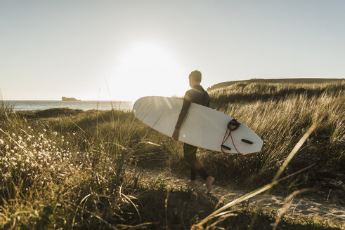 Frankreich, Bretagne, Halbinsel Crozon, Frau geht mit Surfbrett durch die Dünen - UUF08696