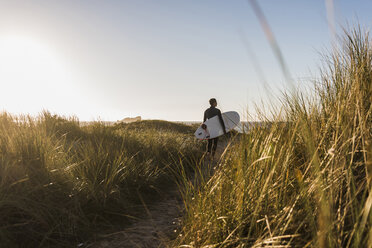 France, Bretagne, Crozon peninsula, woman walking through dunes carrying surfboard - UUF08697