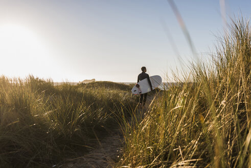 Frankreich, Bretagne, Halbinsel Crozon, Frau geht mit Surfbrett durch die Dünen - UUF08697