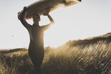 Frankreich, Bretagne, Halbinsel Crozon, Frau geht mit Surfbrett durch die Dünen - UUF08698