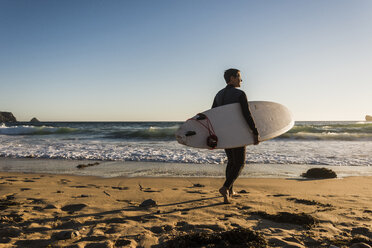 Frankreich, Bretagne, Halbinsel Crozon, Frau geht am Strand mit Surfbrett - UUF08703