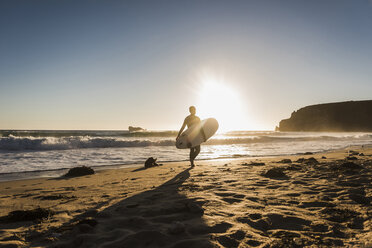 Frankreich, Bretagne, Halbinsel Crozon, Frau geht bei Sonnenuntergang mit Surfbrett am Strand spazieren - UUF08704