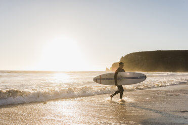 Frankreich, Bretagne, Halbinsel Crozon, Frau geht bei Sonnenuntergang mit Surfbrett am Strand spazieren - UUF08709