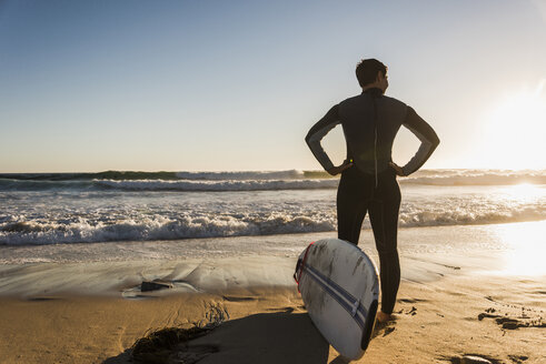 Frankreich, Bretagne, Halbinsel Crozon, Frau bei Sonnenuntergang am Strand stehend mit Surfbrett - UUF08710