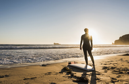 Frankreich, Bretagne, Halbinsel Crozon, Frau bei Sonnenuntergang am Strand stehend mit Surfbrett - UUF08711