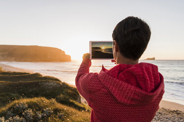 Frankreich, Bretagne, Halbinsel Crozon, Frau an der Küste bei Sonnenuntergang fotografiert mit Tablet - UUF08720