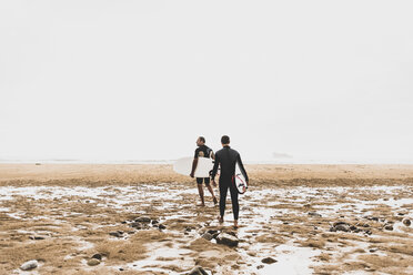 Frankreich, Bretagne, Halbinsel Crozon, Paar geht mit Surfbrettern am Strand spazieren - UUF08730