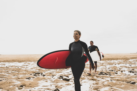 Frankreich, Bretagne, Halbinsel Crozon, Paar geht mit Surfbrettern am Strand spazieren, lizenzfreies Stockfoto