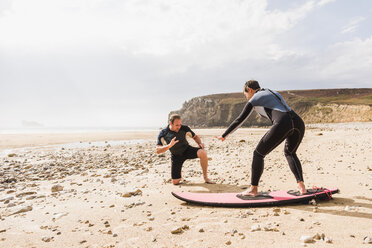 France, Bretagne, Crozon peninsula, man teaching woman surfing on beach - UUF08733