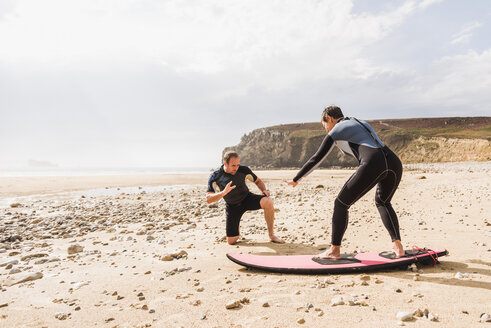 Frankreich, Bretagne, Halbinsel Crozon, Mann bringt Frau am Strand das Surfen bei - UUF08733