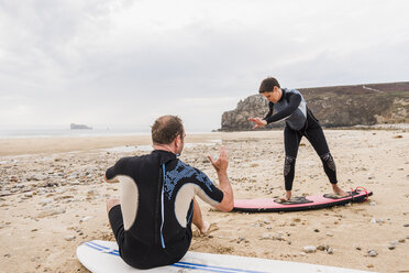 Frankreich, Bretagne, Halbinsel Crozon, Mann bringt Frau am Strand das Surfen bei - UUF08734