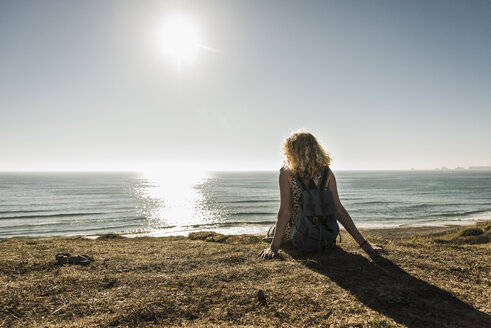 Back view of teenage girl sitting on the beach at evening twilight looking to the sea - UUF08740