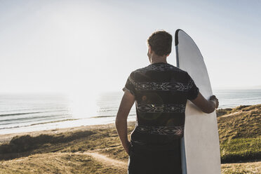 Rückenansicht eines Teenagers mit Surfbrett und Blick auf das Meer - UUF08759