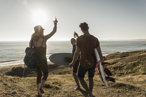 Drei Freunde mit Surfbrettern stoßen am Meer an - UUF08767