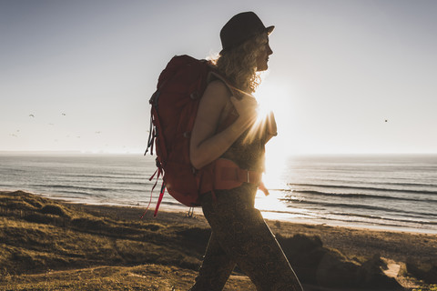 Blondes Teenager-Mädchen mit Rucksack spaziert am Strand in der Abenddämmerung, lizenzfreies Stockfoto