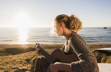Teenager-Mädchen spielt Gitarre am Meer in der Abenddämmerung - UUF08793
