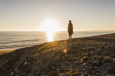 Back view of teenage girl standing on hill at sunset looking to the sea - UUF08795