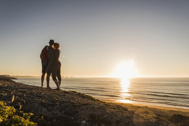 Rückenansicht eines jungen verliebten Paares bei Sonnenuntergang am Meer - UUF08797