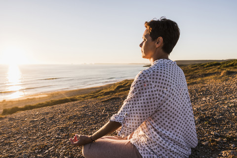 Woman meditating at seaside by sunset stock photo