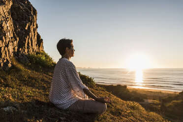 Woman meditating on cliff at sunset - UUF08802