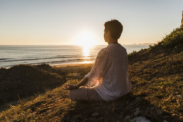 Rückenansicht einer meditierenden Frau bei Sonnenuntergang - UUF08803