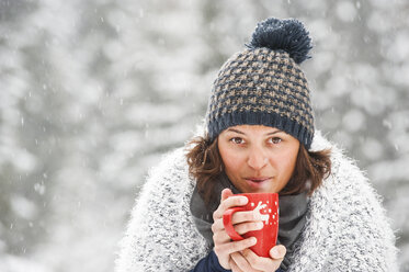 Porträt einer Frau mit Pudelmütze, die eine Tasse mit einem heißen Getränk im Winter hält - HHF05426
