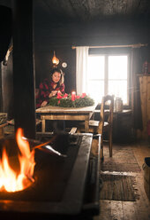 Woman in a wooden hut lighting candle on Advent wreath - HHF05429