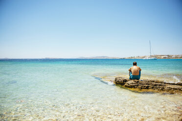 Griechenland, Koufonissi, Mann sitzt auf einem Felsen und schaut auf das klare Wasser des Ägäischen Meeres - GEMF01156