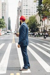 Indischer Geschäftsmann in Manhattan steht auf einem Zebrastreifen und hält ein Smartphone in der Hand - GIOF01511