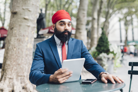 Indischer Geschäftsmann, der in Manhattan sitzt und ein digitales Tablet benutzt, lizenzfreies Stockfoto