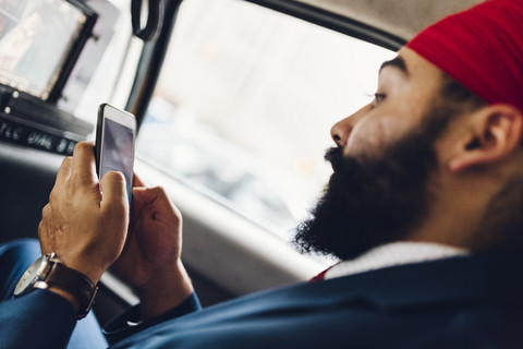 Indischer Geschäftsmann benutzt Smartphone im Taxi, lizenzfreies Stockfoto