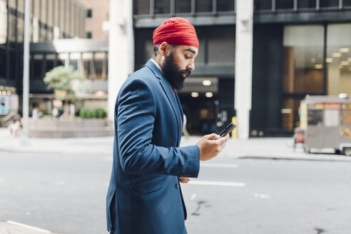 Indian businessman in Manhattan using smartphone, walking in the street - GIOF01549