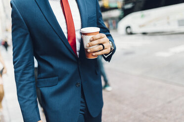 Geschäftsmann beim Spaziergang in der Stadt, mit einer Tasse Kaffee in der Hand - GIOF01557