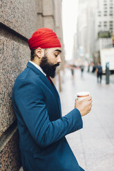 Indischer Geschäftsmann in Manhattan, der an der Wand lehnt und Kaffee trinkt - GIOF01559