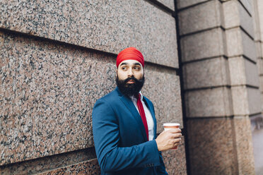 Indian businessman in Manhattan leaning against wall, drinking coffee - GIOF01560