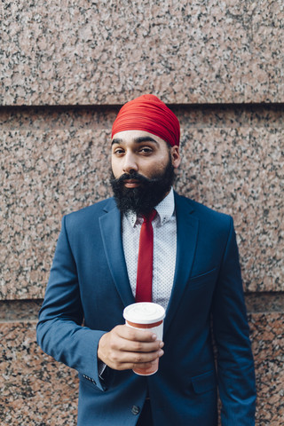 Indischer Geschäftsmann in Manhattan, der an der Wand lehnt und Kaffee trinkt, lizenzfreies Stockfoto