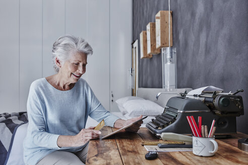 Lächelnde ältere Frau beim Online-Shopping im Schlafzimmer - RORF00308