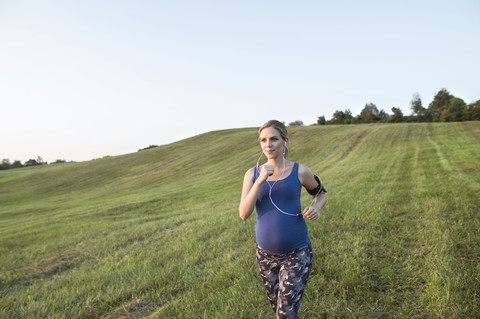 Schwangere Frau joggt im Feld, lizenzfreies Stockfoto
