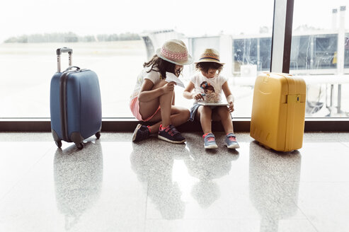 Zwei kleine Mädchen warten am Flughafen und spielen mit einem digitalen Tablet - MGOF02518