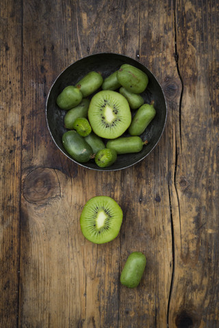 Schale mit geschnittenen und ganzen Kiwis und geschnittenen Kiwis auf dunklem Holz, lizenzfreies Stockfoto