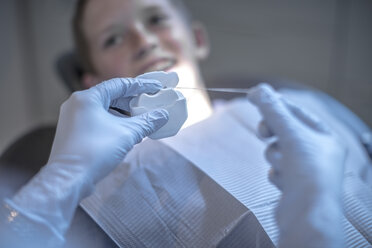 Zahnarzt hält Zahnseide mit einem Jungen in einer Zahnarztpraxis im Hintergrund - ZEF10650